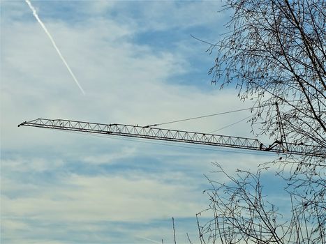 Crane behind trees in front of blue sky with clouds