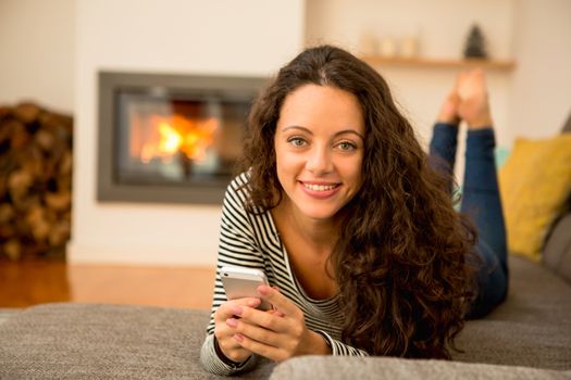 Beautiful woman using a cellphone at home at the warmth of a fireplace