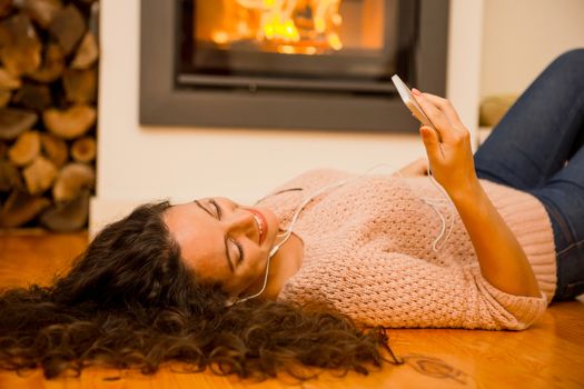 Beautiful woman listen music at home at the warmth of a fireplace