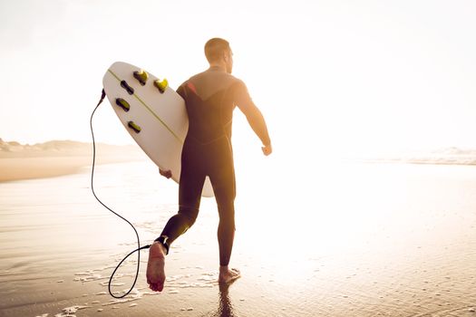 A surfer with his surfboard running to the waves