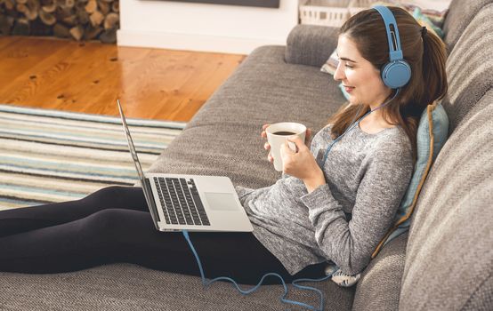 Beautiful woman working at home with a laptop while listen music and drinking coffee