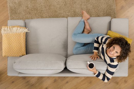 Top view of a beautiful woman on the sofa and drinking coffee