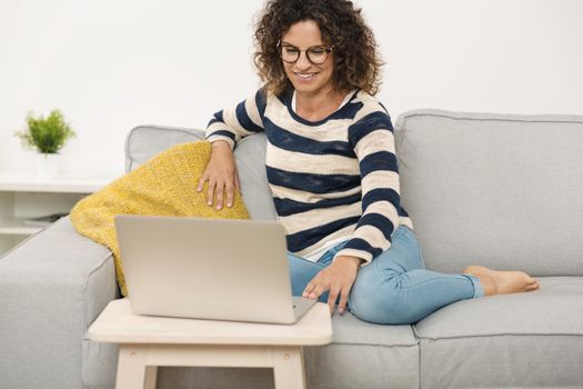 Beautiful woman at home sitting on the sofa and working with a laptop