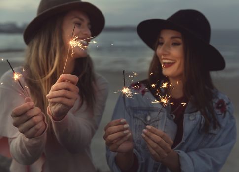 Two best friends celebrating, holding sparklers at beach 