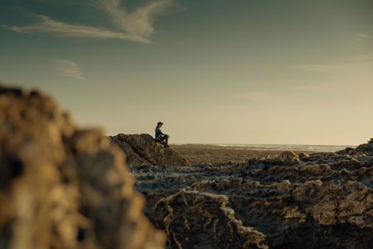 Beuutoful woman alone in the beach sitting on the rocks