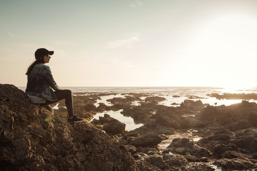 Beuutoful woman alone in the beach sitting on the rocks