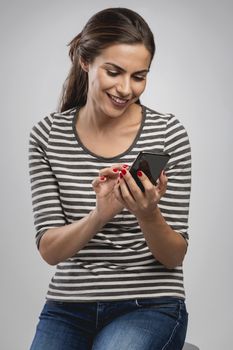 Beautiful happy young woman sitting on a bench and sending a text message to someone