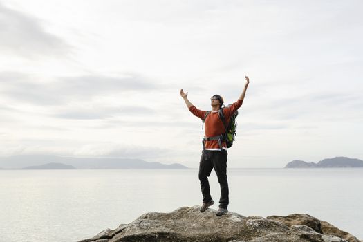 Man with backpack and arms raised  enjoying the beautiful morning view of the coast