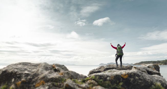 Woman with backpack and arms raised  enjoying the beautiful view of the coast