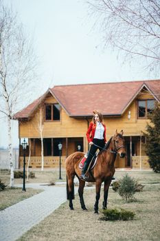 red-haired jockey girl in a red cardigan and black high boots with a horse for a walk