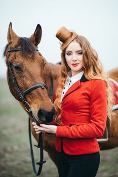 red-haired jockey girl in a red cardigan and black high boots with a horse for a walk