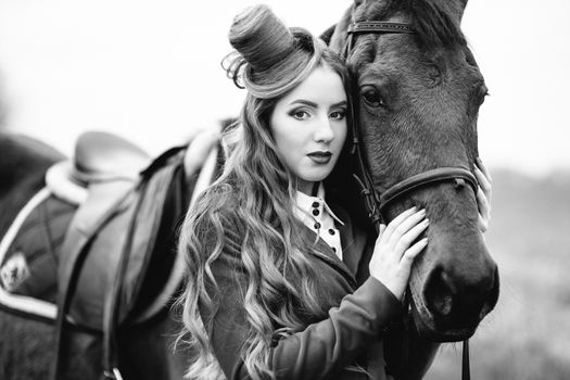 red-haired jockey girl in a red cardigan and black high boots with a horse for a walk