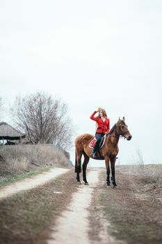 red-haired jockey girl in a red cardigan and black high boots with a horse for a walk