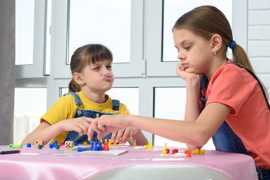 Girl playing a board game teases another girl