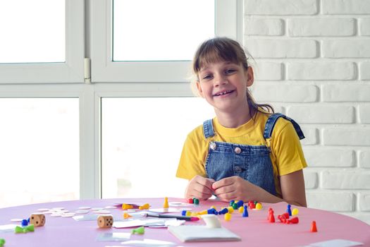 Cheerful girl plays board games at the table and looked into the frame