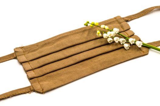 Still life of a brown facial mask with a sprig of lily of the valley on a white background anti covid 19, DIY sewing project