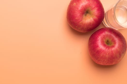 red apple and glass of water isolated on orange background, healthy food and fitness concept