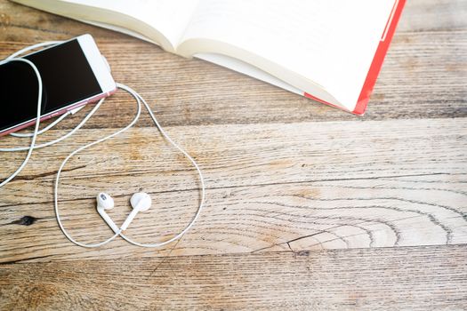 white heart shape earphone with smartphone and open book on working table top view with copy space