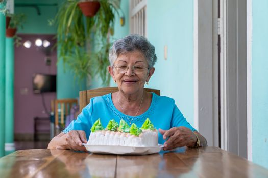 Elderly wrinkled woman sitting and a cake on table