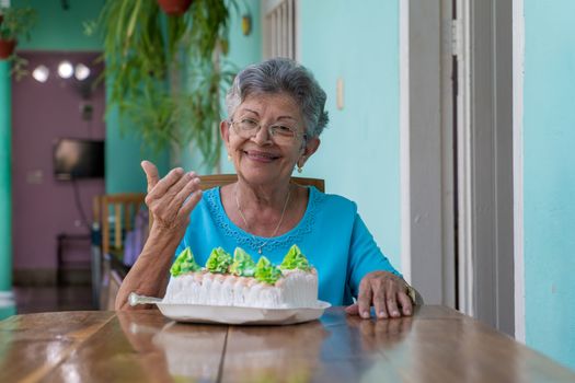 Elderly wrinkled woman sitting and a cake on table