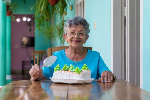 Elderly wrinkled woman sitting and a cake on table