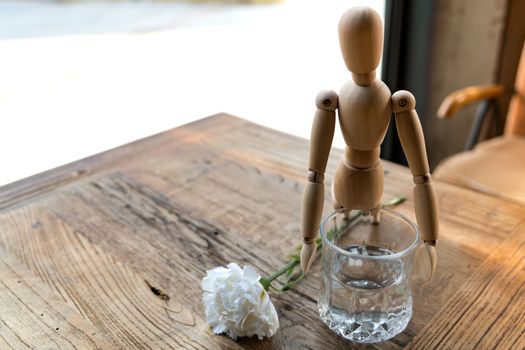 wood man is trying to hold on a glass with white carnation on the wooden table