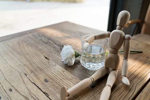 a wood man is sitting and put the arm on the glass of water