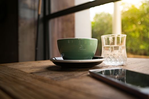 A coffee cup and a glass of water with the smart phone on the wooden table