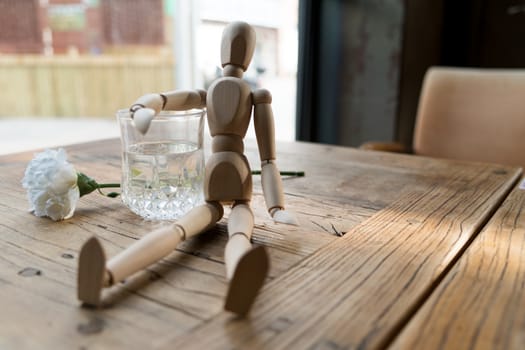 a wood man is sitting and put the arm on the glass of water