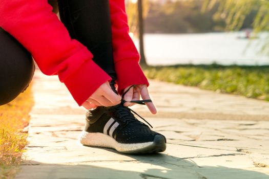 close up young woman tying shoelace while walking, sunny day in winter season