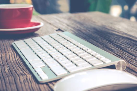 focus on English alphabet of the while keyboard with mouse and red cup of coffee