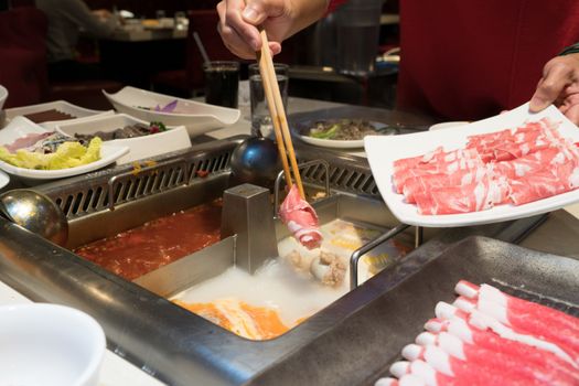 a red shirt women is cooking the Chinese shabu hotpot