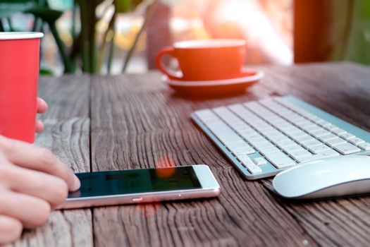 soft focus on the hand touching the smart mobile phone on the working table with red cup of coffee