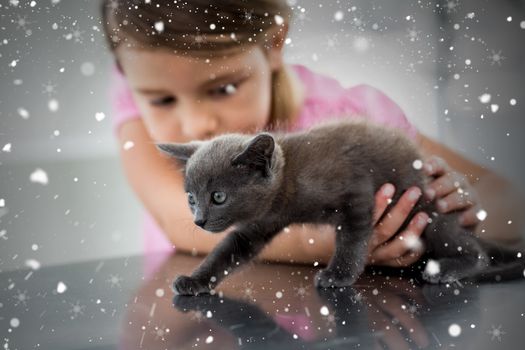 Composite image of girl playing with kitten against snow falling