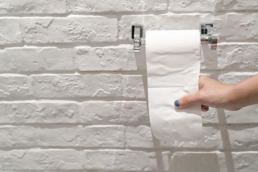 female hand pulling a white tissue paper from tissue roll in the restroom.