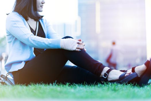 wrist hand pain women sit on the green grass in the playground on sunset, city lifestyle concept