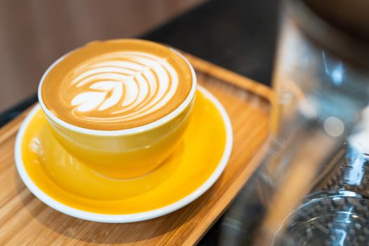 Latte art coffee cup in yellow glass on wooden plate