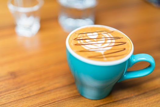 Latte art coffee cup in green glass on wooden table