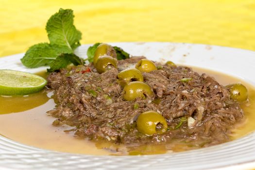 Veal ripped meat served in a white dish marinated with olives, and a slide of lemon