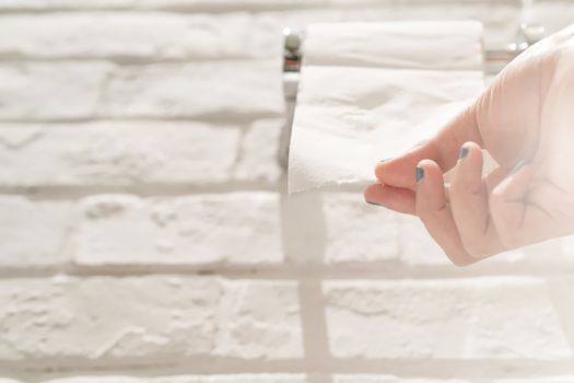 female hand pulling a white tissue paper from tissue roll in the restroom.