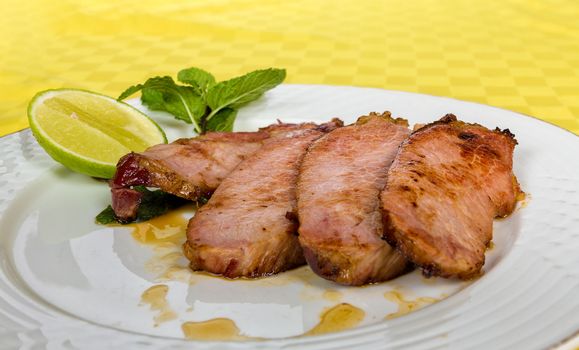 Four slide of grilled smoked pork served in a white dish and a lemon slide