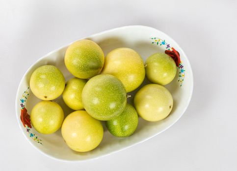 A group of ten passion fruit in a bowl on a white background