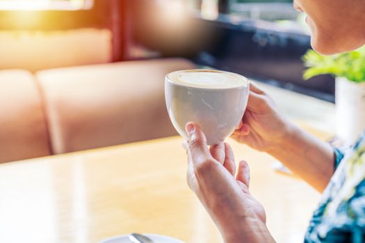 women hands holding hot cup of coffee or tea in morning sunlight