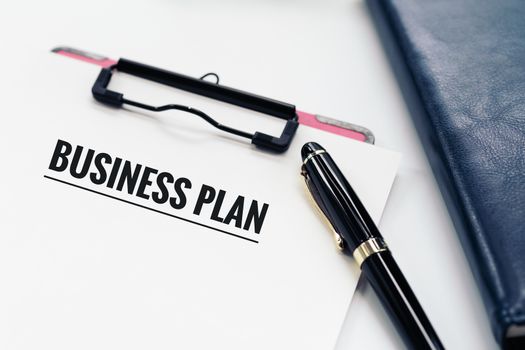 Business plan concept, pen and clipboard with word Business plan, glasses and diary book on white background with copy space