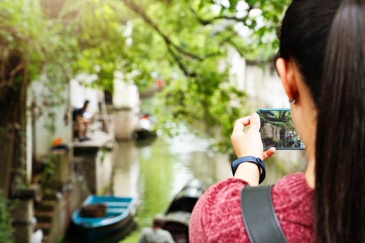 young woman having fun in local canal city in China with camera on smartphone making pictures