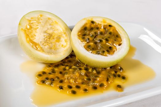 Two halve of a passion fruit one empty and other full of seeds in a white bowl