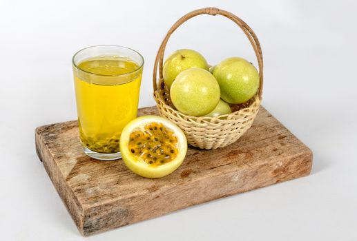 A glass of passion fruit juice, a basket with a group of passion fruits and a half maracuya, all this on a piece of wood.