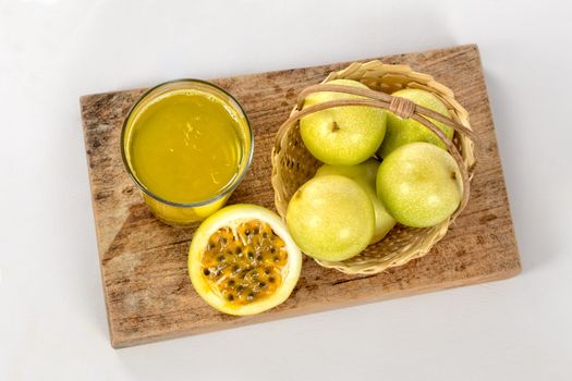 A glass of passion fruit juice, a basket with a group of passion fruits and a half maracuya, all this on a piece of wood.