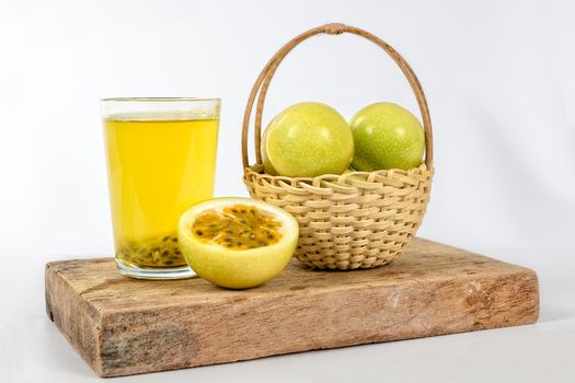 A glass of passion fruit juice, a basket with a group of passion fruits and a half maracuya, all this on a piece of wood.