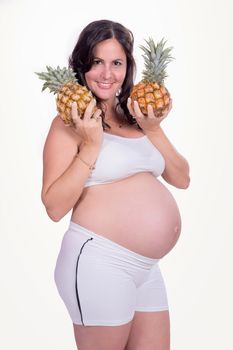 A pregnant woman with to pineapple in her hands wearing white clothes.